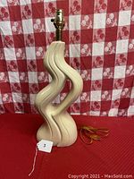 Front view of mid-century modern ceramic table lamp with curved amorphous shape on red textured surface and red-and-white checkered background.