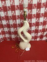 Front view of mid-century ceramic table lamp with curved, wavy amorphous body in cream color against red and white checkered background.