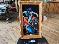 Full front view of the mid-century oil on velvet bullfighting painting, showing the matador in blue and green attire with a red cape, framed with carved wood.