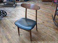 Side view of Mid-Century Danish inspired wooden chair with black vinyl seat showing curvature of backrest and seat condition.