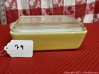 Side view of the large yellow Pyrex refrigerator dish with clear glass lid, showing handles and rectangular shape.