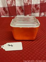 Front view of small red Pyrex refrigerator dish with lid showing square shape and red color with wear