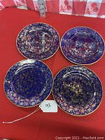 Set of four cobalt blue plates with gold gilt floral decoration arranged on red surface.