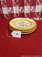 Five stacked yellow rimmed dinner plates with a hand-painted yellow tulip floral design on a checkered tablecloth.