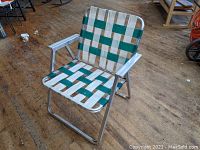 Front angle view of the vintage lawn chair showing green and white woven webbing seat and back, and aluminum frame with armrests.