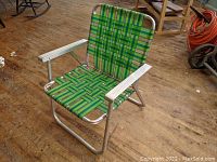 Front and side view of the green webbed aluminum folding lawn chair on wooden floor.