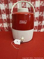 Front view of vintage Coleman insulated water jug showing red and white colors, handle, lid, and spigot.