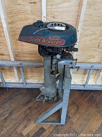 Full side view of vintage Scott-Atwater outboard motor with dark blue and red painted top housing and metal lower housing, mounted on a metal frame for display.