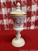 Front view of tall milk glass candy jar with hobnail base and floral decoration with gold trim, lid in place.