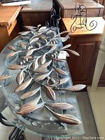 Metal leaf and berry wall art piece with a copper-tone finish, placed on a reflective glass surface.