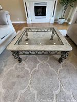 Glass and travertine coffee table with metal base viewed in living room between sofas on a carpet