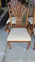 Front view of a wooden dining chair with carved backrest and light cloth upholstered seat