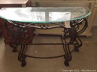 Clear view of the half-moon shaped glass top on wrought iron base with ornate scroll design from front angle.