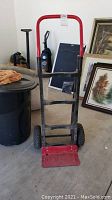 Full front view of the Milwaukee hand truck showing red frame, black wheels and base plate, black handles.