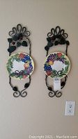 Pair of metal wall art holders with decorative fruit motif plates mounted on wall.