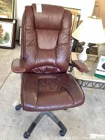 Full view of brown leather office chair with padded armrests and seat on black wheeled base.