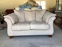 Front view of a beige loveseat showing fabric upholstery, plush back cushions, two seat cushions, rolled arms, and wooden feet.