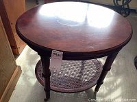 Round wooden corner table angled view showing spindle legs and caned lower shelf with some visible surface scratches