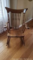 Front view of vintage wooden rocking chair showing carved top rail, spindle back, armrests, and seat with wear.