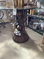 Full view of the vintage metal table with clear glass top showing scrollwork base and decorative central plant design