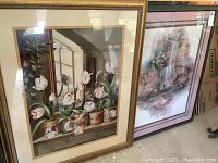 Photo showing two framed paintings side by side on the floor. One painting of white tulips in pots by window. The other painting shows a waterfall flowing over rocks.