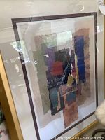 Full view of the framed abstract mixed media artwork showing layered torn paper elements in varied colors with glass reflection.