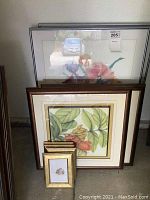 Photo showing multiple framed floral prints, different sizes, stacked leaning against the wall
