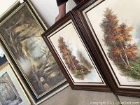 Three framed paintings: two autumn tree water scenes and one forest landscape