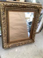 Frontal photo of rectangular wall mirror showing ornate carved gold frame with floral and leaf details.