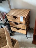 Front angle view of the wicker shelf unit showing all three drawers and black metal frame.