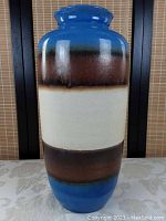 Full front view of the tall ceramic vase showing the color bands and glossy finish.