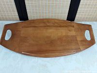 Photo showing top view of teak wooden tray shaped like a surfboard, with handles and smooth wood grain.