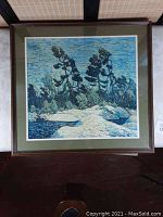 Framed art print of a landscape by Tom Thomson showing blue sky, pine trees, and rocks by water, in a wooden frame with green mat.