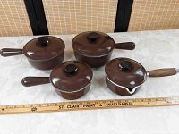 Overview of four brown enamel pots with lids and handles, ruler for scale