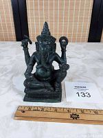 Front view of the vintage cast iron Ganesha statue showing seated figure with multiple arms, elephant head with trunk, high conical crown, and base with ruler for scale.
