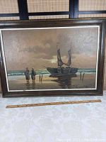 Full view of the framed oil painting depicting a fishing boat at shore with two women carrying baskets, showing the composition and frame.