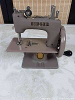 Front-left view of the small Singer miniature sewing machine showing brand name and sewing needle section.