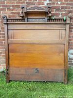Full view of the antique wooden headboard showing the overall size and shape, placed against a brick wall.