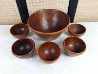 Photo showing full set of one large wooden salad bowl surrounded by five smaller wooden salad bowls on a white patterned cloth background with a decorative screen behind.