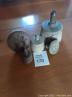 Photo showing all five wooden butter prints of varying sizes with carved tops, showing wear and age marks, placed on wooden floor surface.