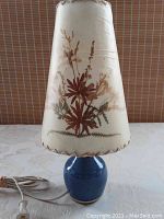 Front view of Dornbusch lamp showing blue pottery base with attached cord and floral cream shade with stitched edges.