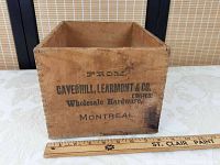 Front view of rectangular wooden box with black printed text showing company name and location, with a ruler for scale.