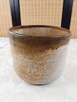 Front view of cylindrical pottery flower pot holder showing splatter glazing in brown and off-white tones