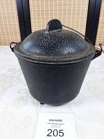 Front view of the older cast iron pot with lid in place, showing three short legs at the base and a wire handle on top.