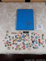 Photo showing a blue album and a variety of loose vintage stamps spread on a white surface.