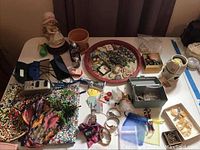 Overview of the lot showing most jewelry pieces, figurine, platter, fabric items, glasses cases, and small boxes scattered on a table
