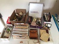 Photo of multiple boxes of vintage envelopes, papers, recipes, diary, leather pouch, and small desk accessories arranged on a table.