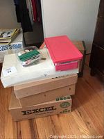 Stacked sealed boxes including Excel box, white large box and two plastic containers on top, indicating stored sewing supplies