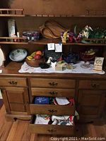 Full view of wooden hutch with drawers open showing various decorative and household items including artificial fruit bowl, floral arrangements, teapot, ceramic birds, linens.