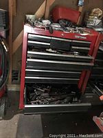 Front view of red Craftsman tool cabinet showing multiple open drawers with various hand tools and sockets inside.